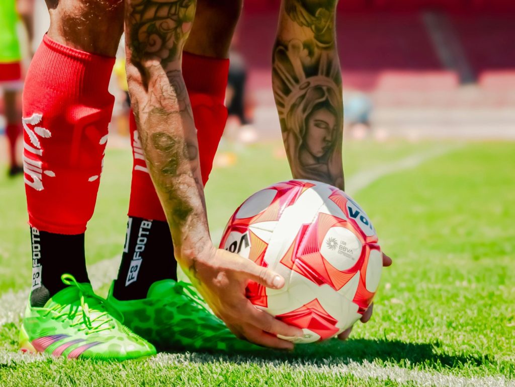 Primer plano de los brazos tatuados de un futbolista colocando el balón para un tiro libre.